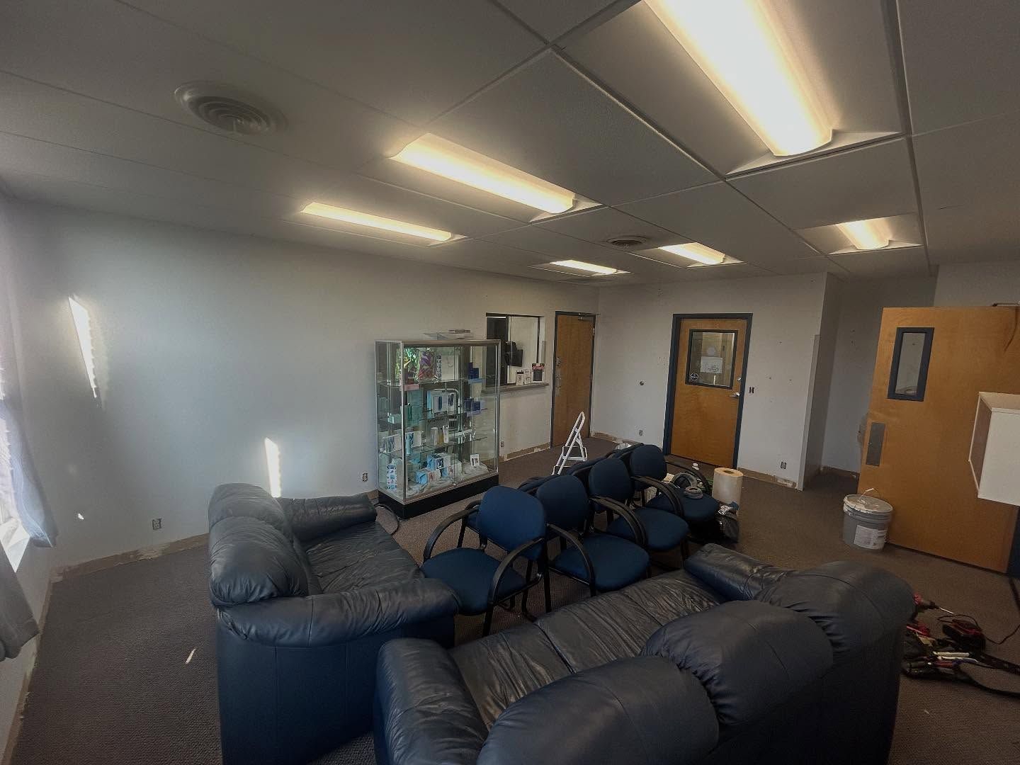 Spacious room with a black leather couch, chairs, display case, and bright overhead lights.