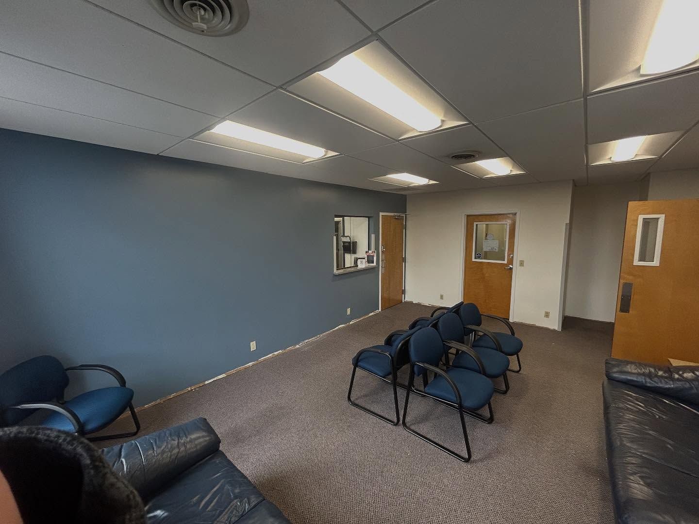 Waiting room with blue chairs, blue wall, brown carpet, and bright ceiling lights.