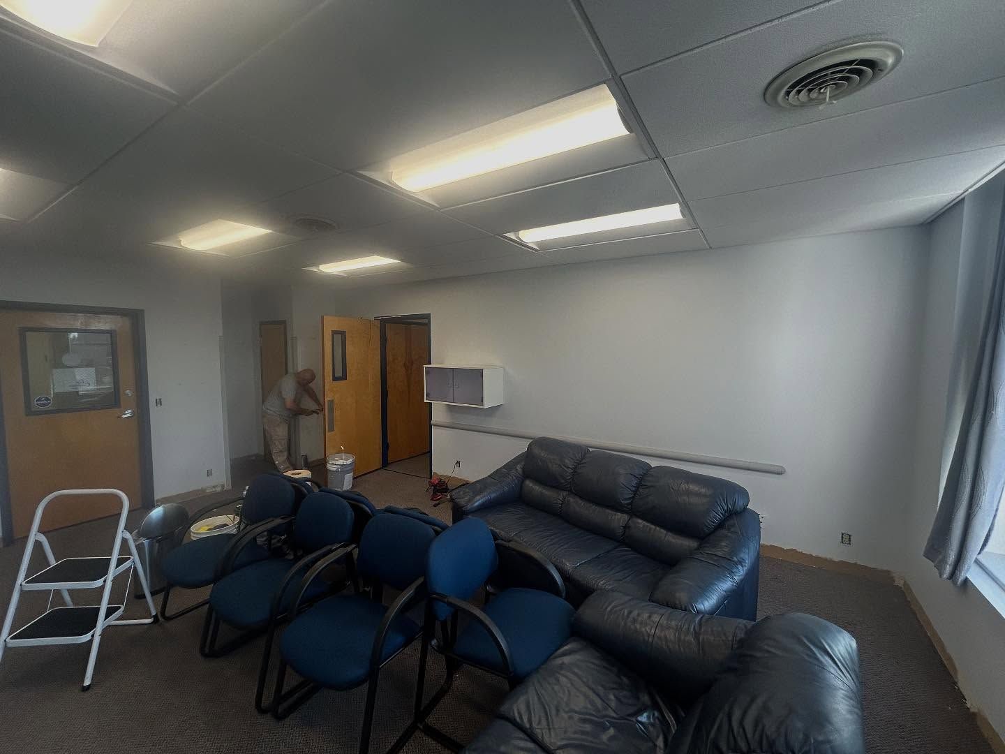 An empty room with blue chairs and a leather couch. A ladder and doors are visible.