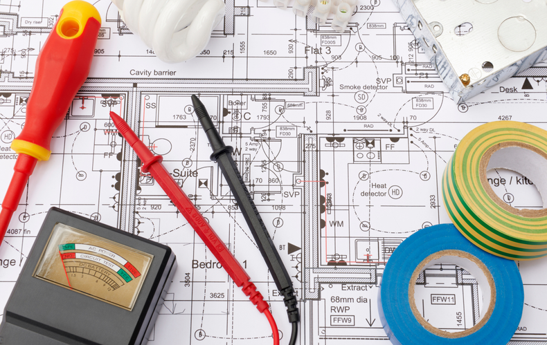 Electrical tools on blueprint: screwdriver, multimeter, probes, tape rolls, and lightbulb.