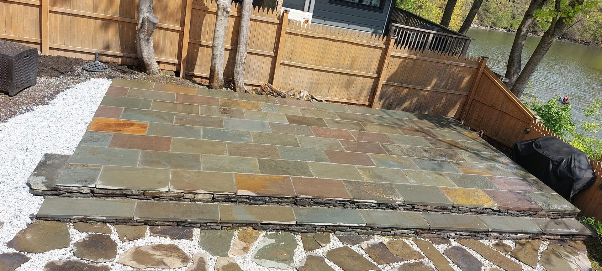 Patio with slate tiles and river view. White stone border. Wooden fence.