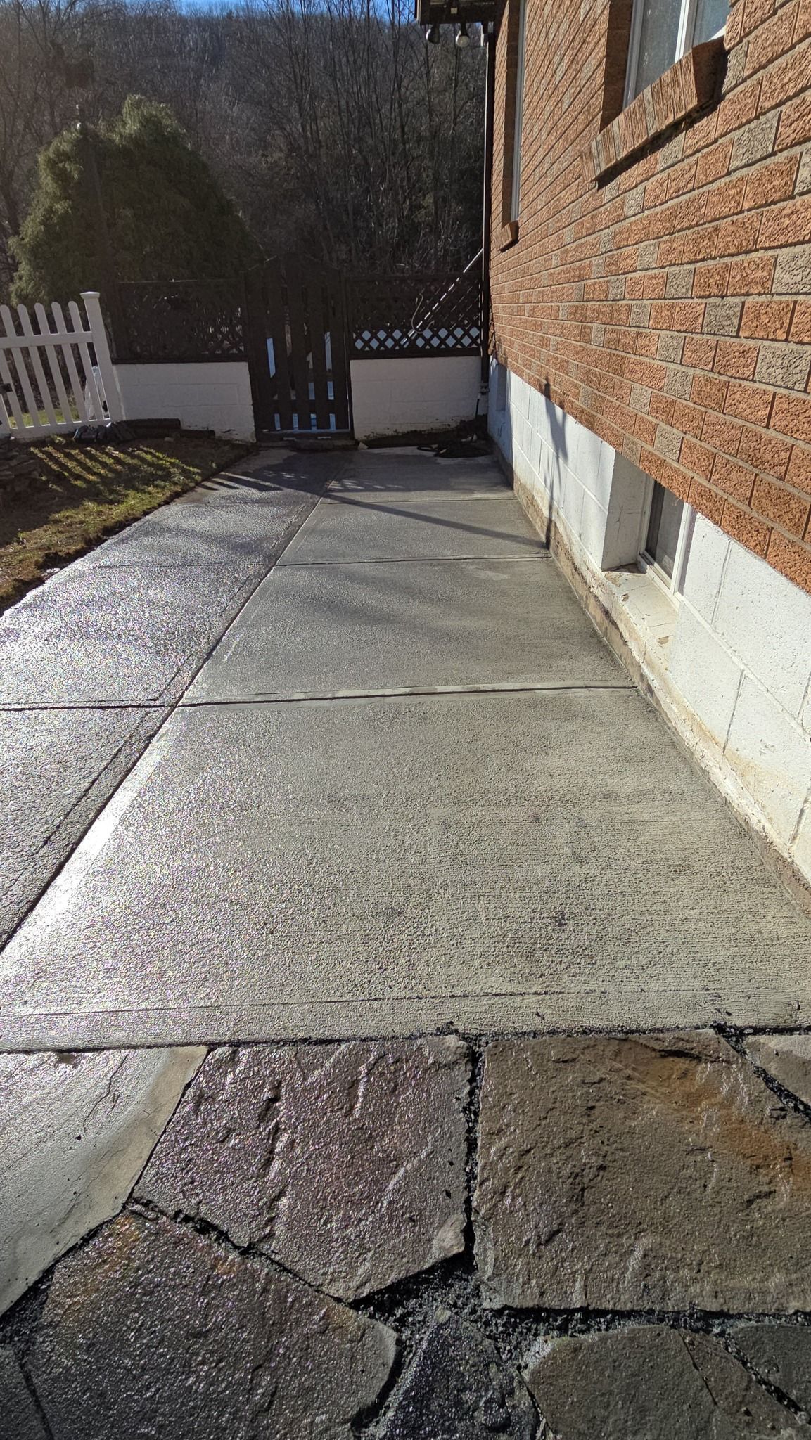 Concrete walkway next to a brick building leads to a gated area.