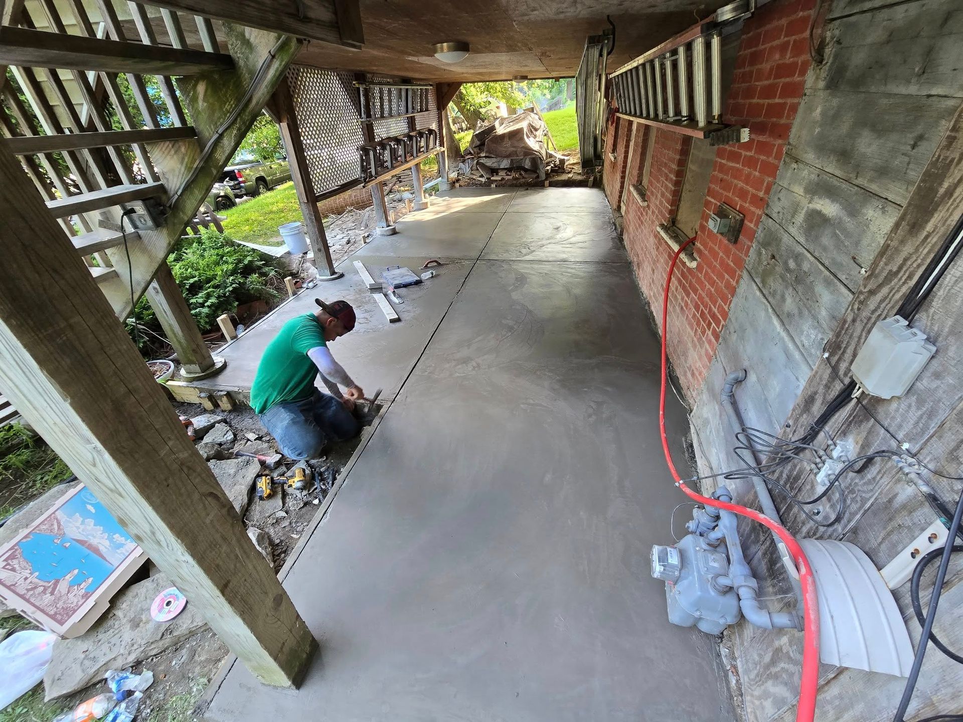 Person kneeling, applying sealant to a newly poured concrete walkway, next to a brick building.