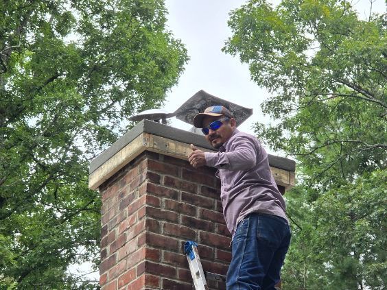 Man on a ladder by a brick chimney giving a thumbs up. He's wearing sunglasses. Green trees in the background.