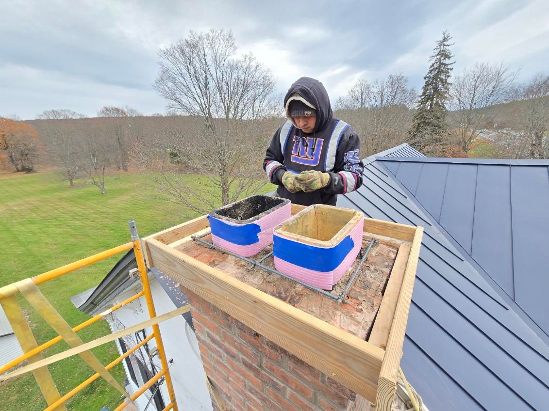 Person on a roof working on a chimney with a wooden frame and two colorful coverings.