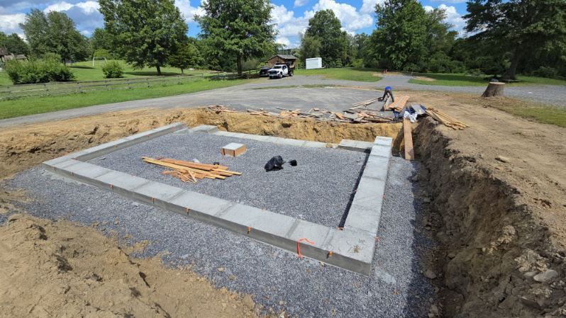 Foundation for a building, with concrete blocks forming a rectangle within a gravel-filled trench.