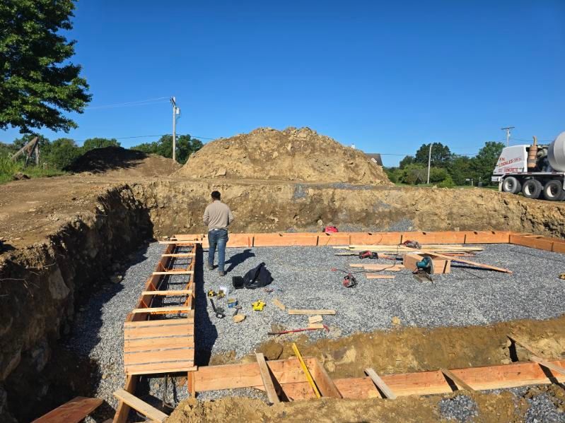 A worker is standing inside the form. A pile of dirt and a concrete truck are in the background.