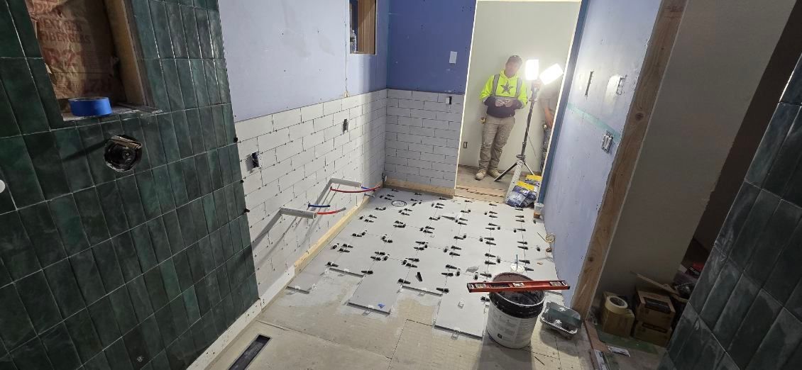 Bathroom under construction with green tile, blue wall, and worker.