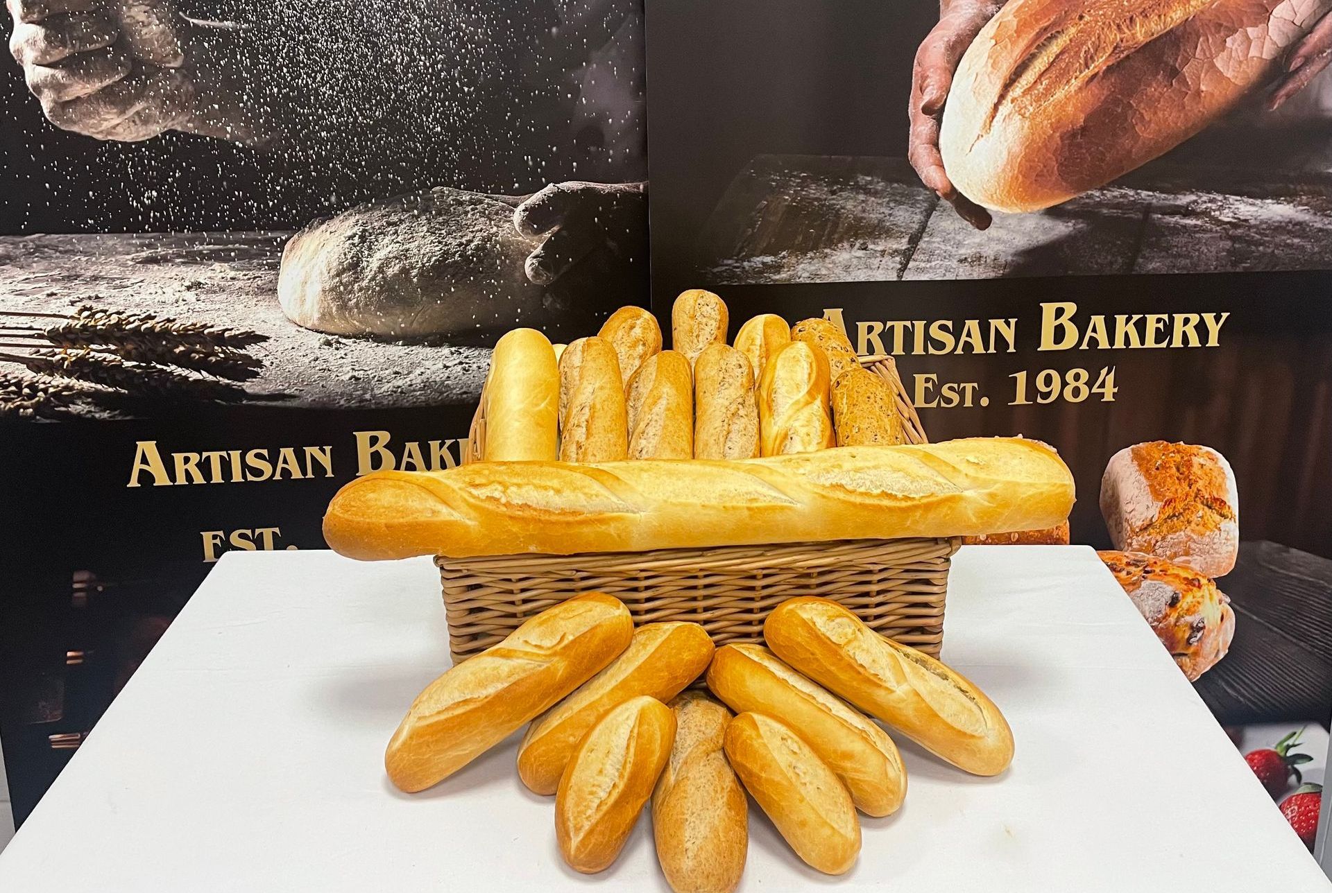 A basket of bread sits on a table in front of a sign that says artisan bakery