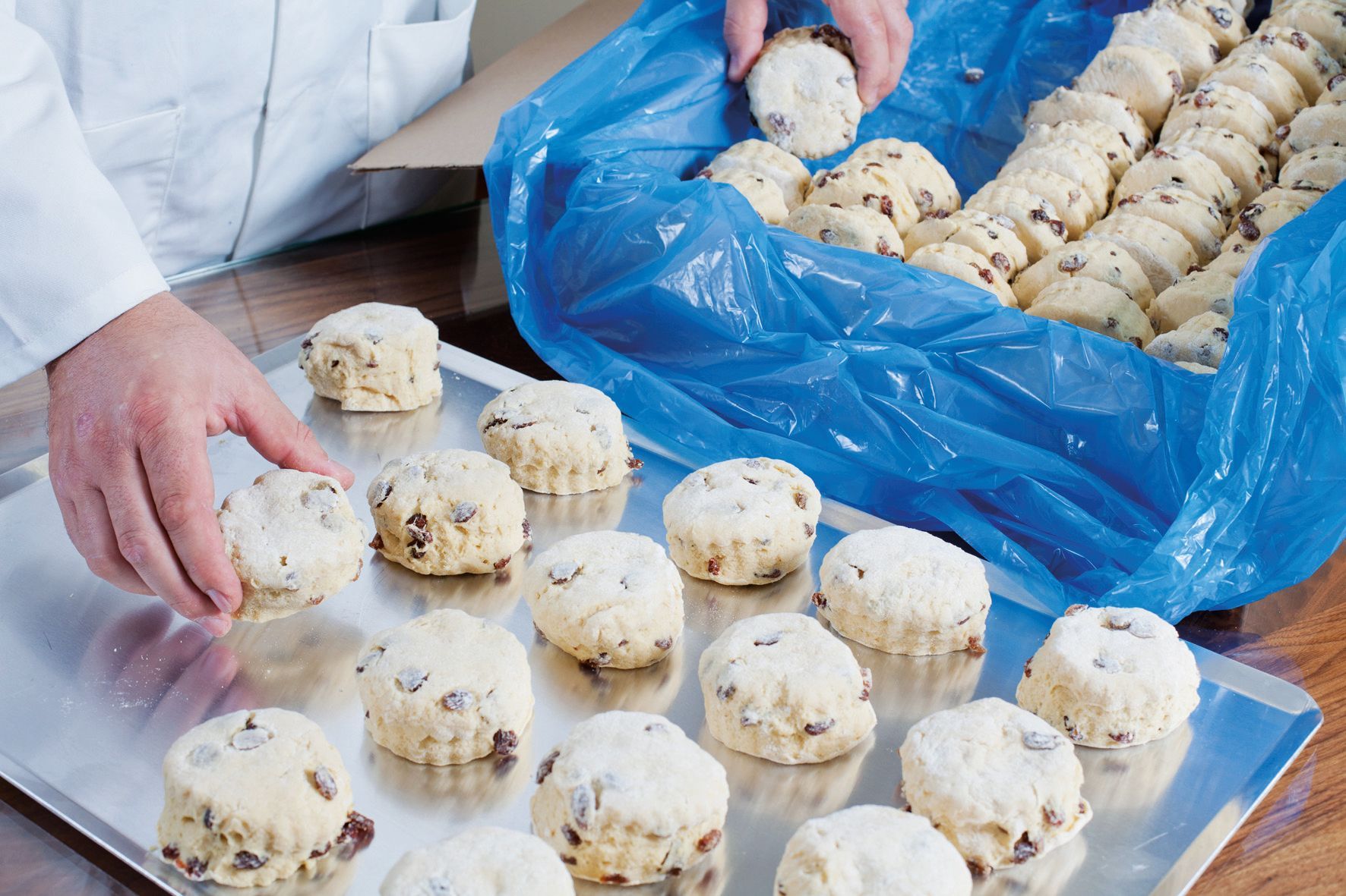 A person is putting cookies on a tray next to a bag of cookies.
