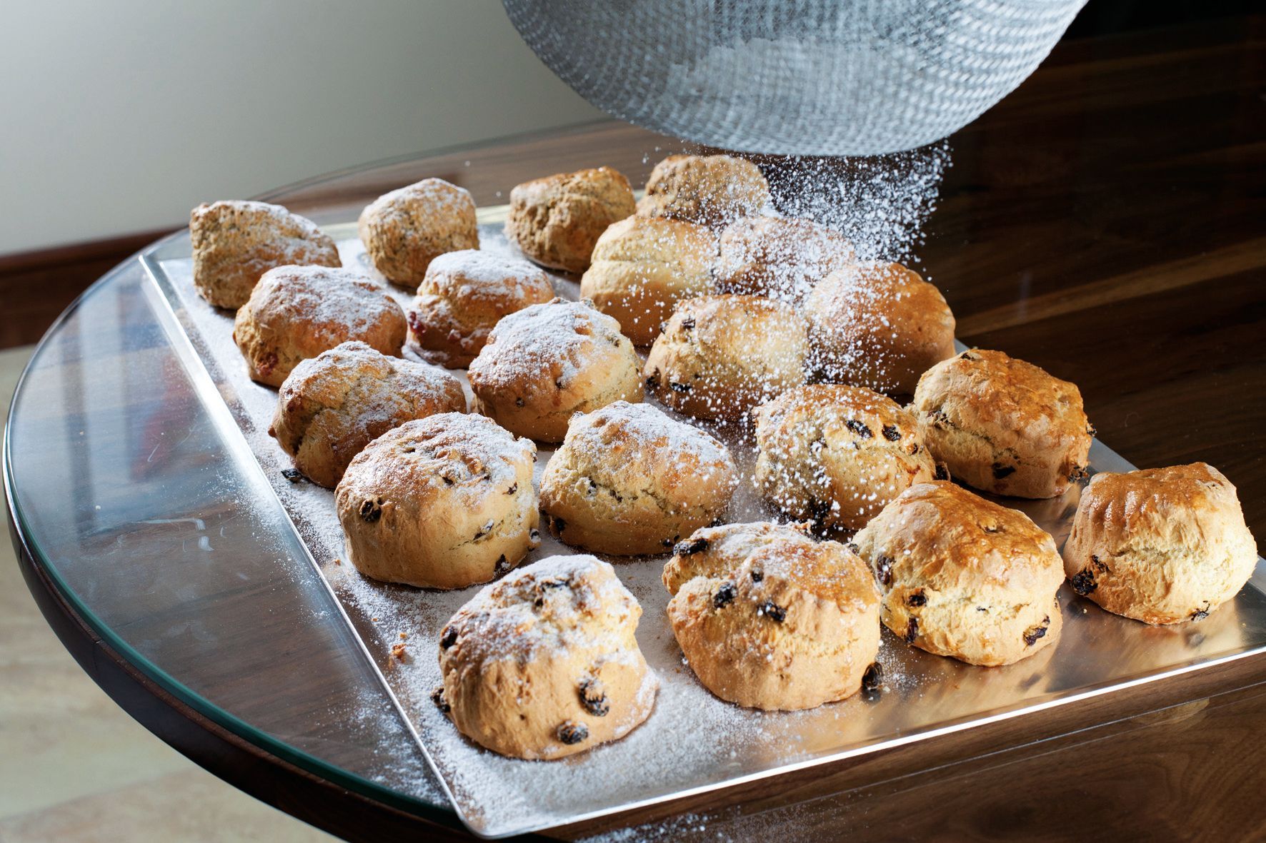 Powdered sugar is being poured on a tray of scones