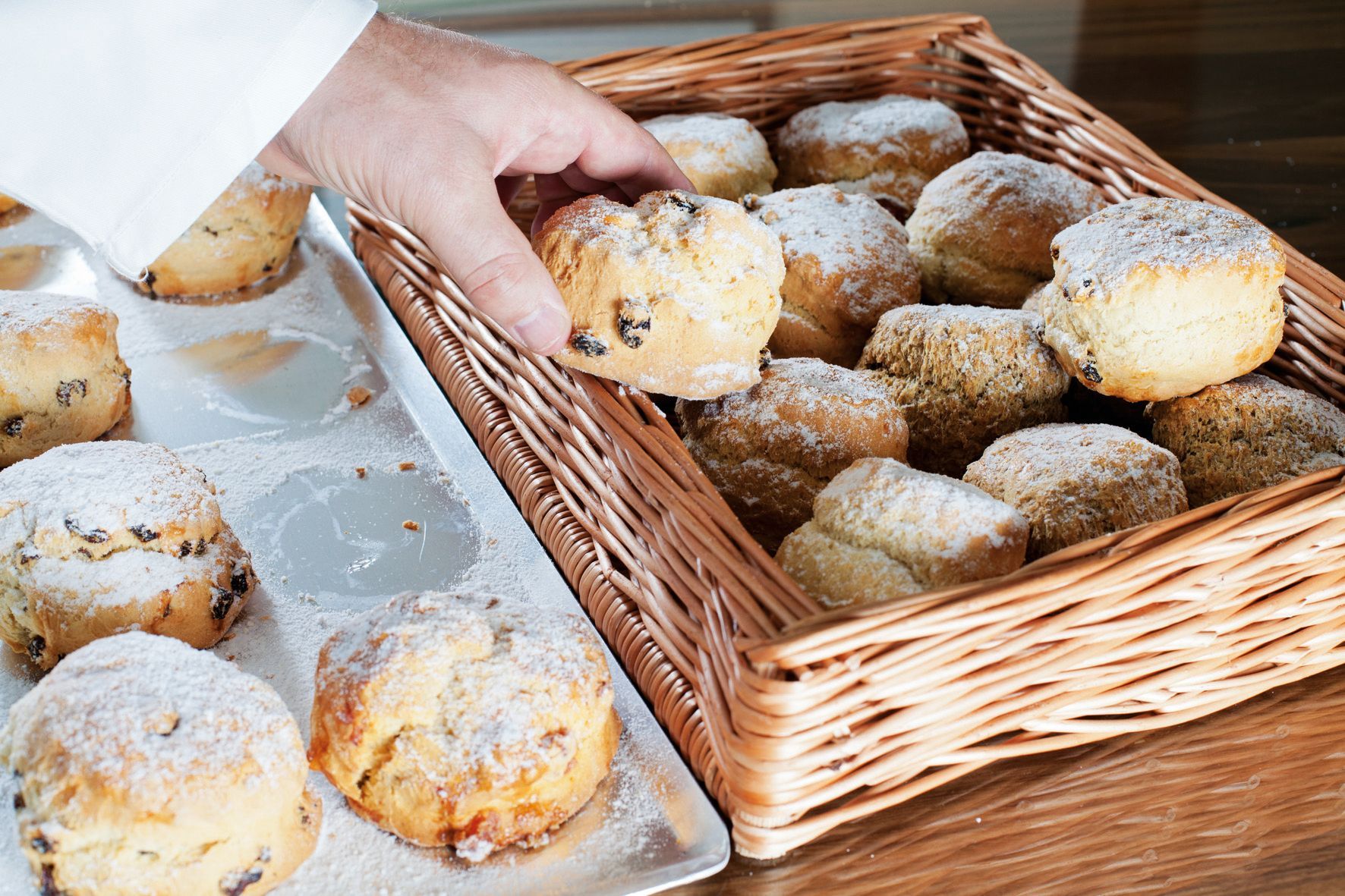 A person is taking a pastry out of a basket of pastries.