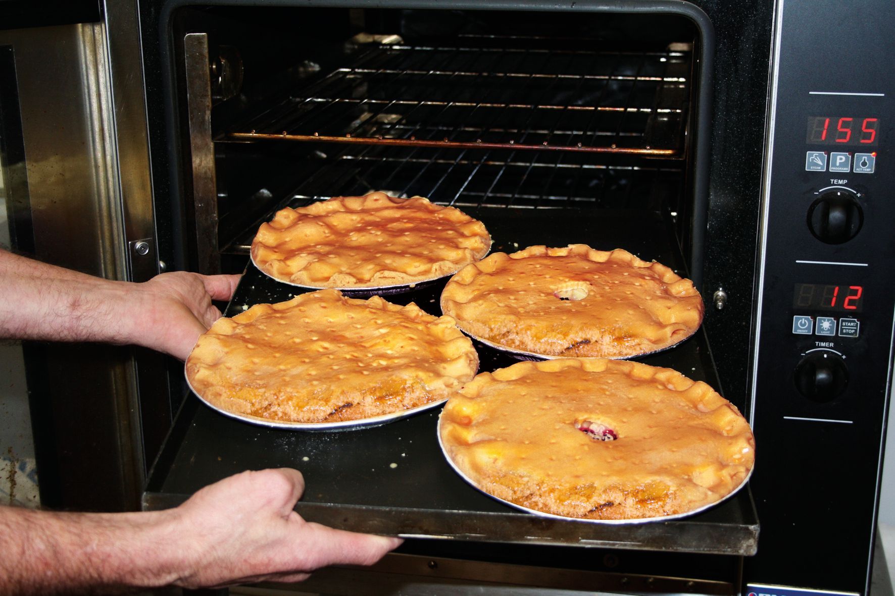 Four pies are being pulled out of an oven with a digital display that reads 11:39