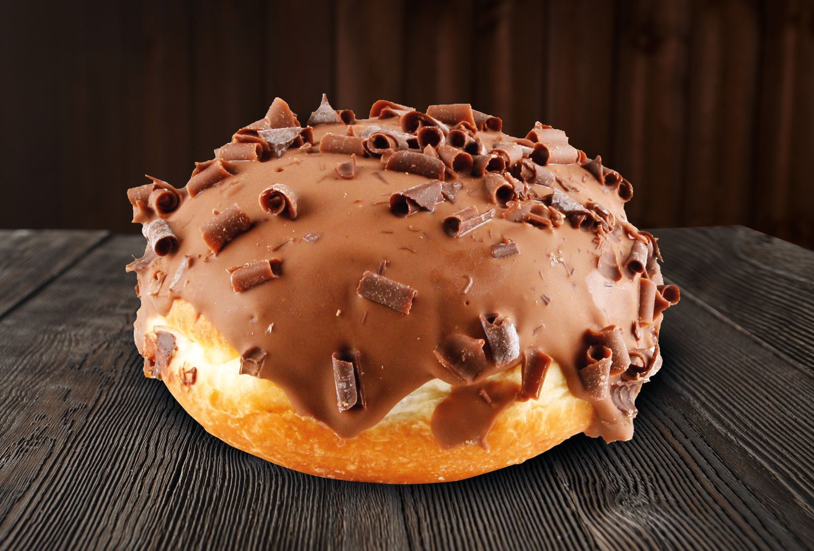 A chocolate donut is sitting on a wooden table.