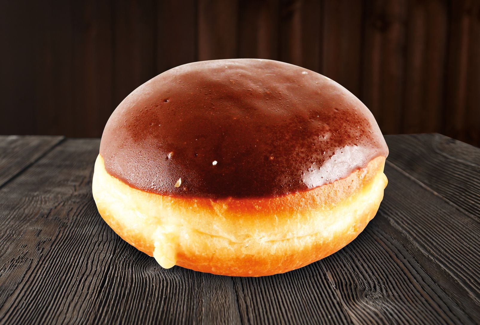 A chocolate donut is sitting on a wooden table.
