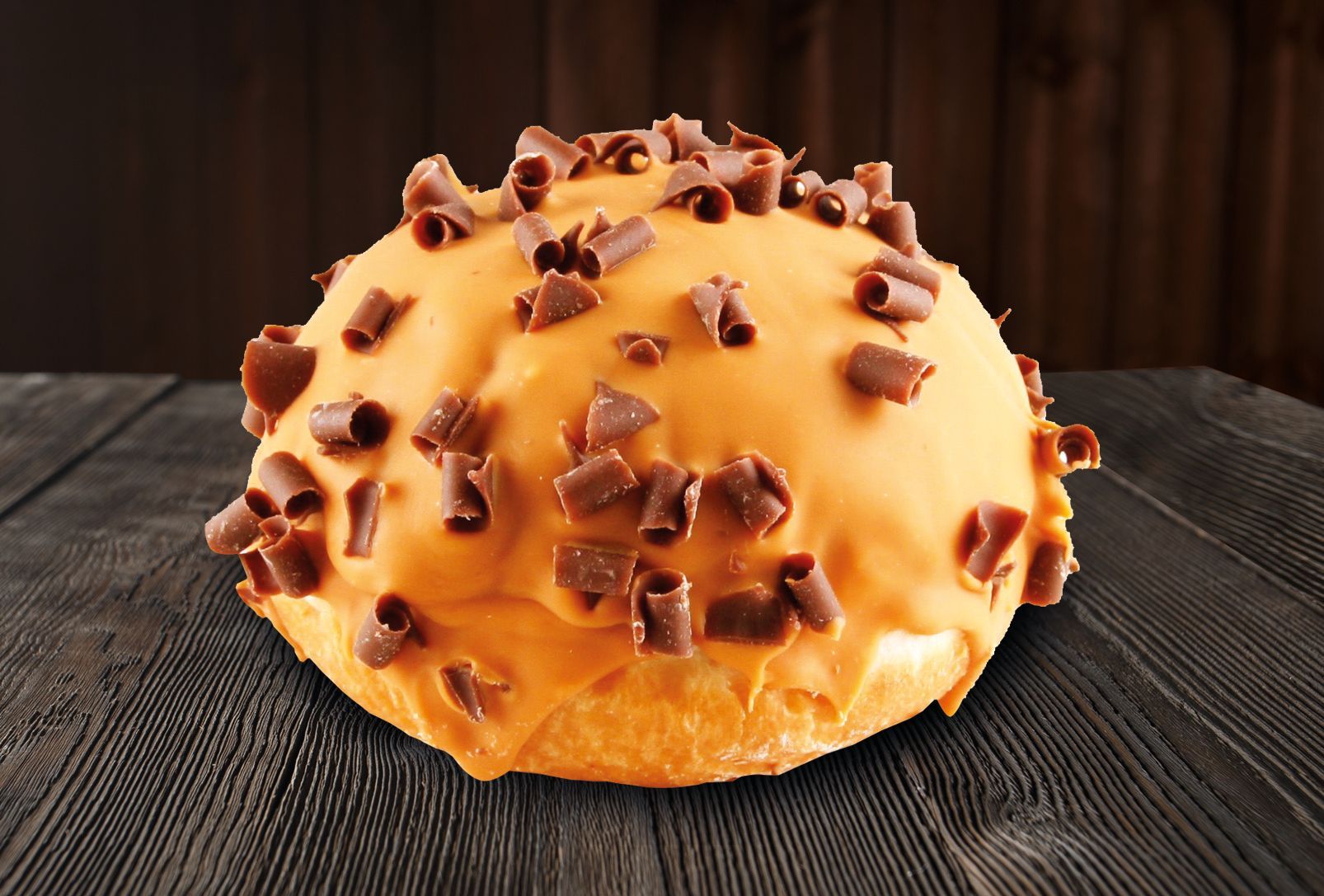 A donut with chocolate shavings on top is sitting on a wooden table.