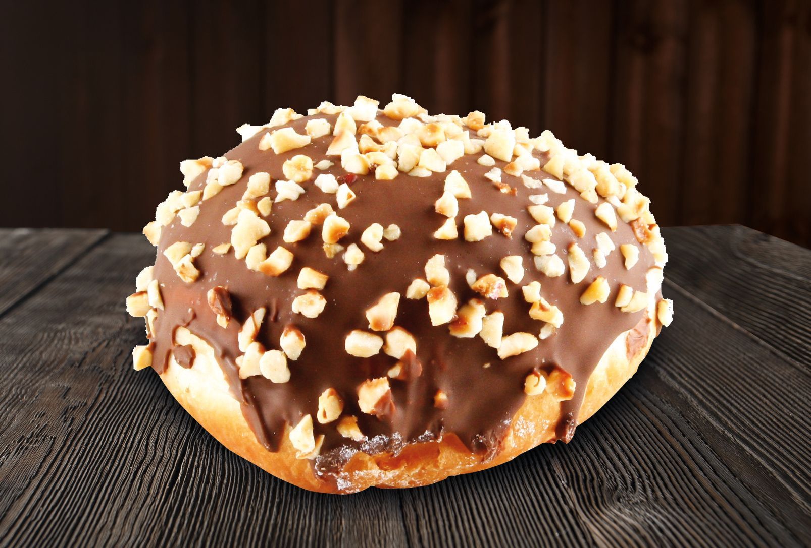 A chocolate donut with nuts on top is sitting on a wooden table.