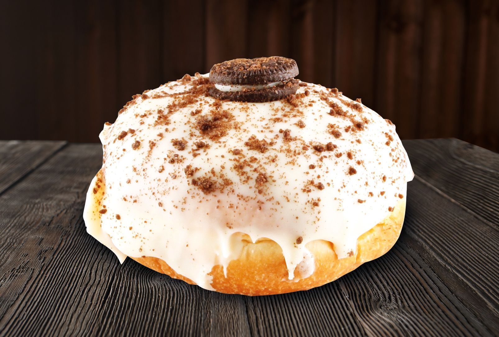 A donut with white frosting and chocolate sprinkles on top is on a wooden table.