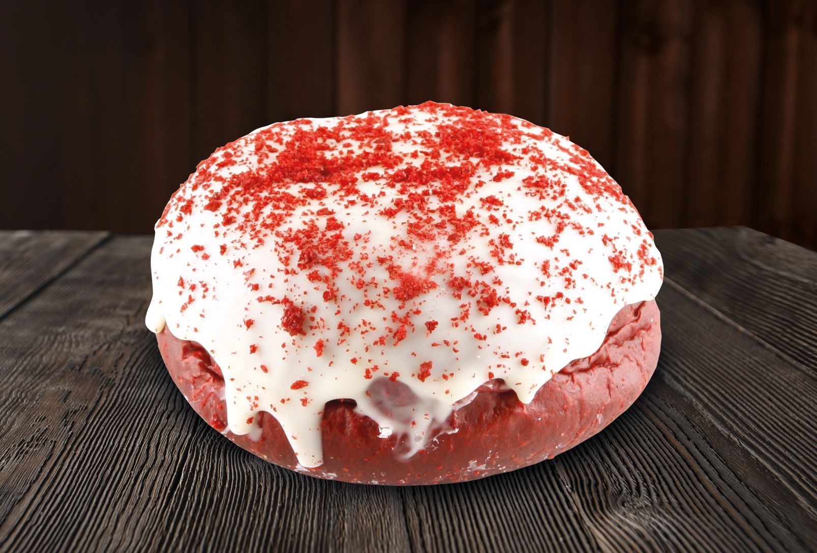 A red velvet donut with white frosting and red sprinkles on a wooden table.