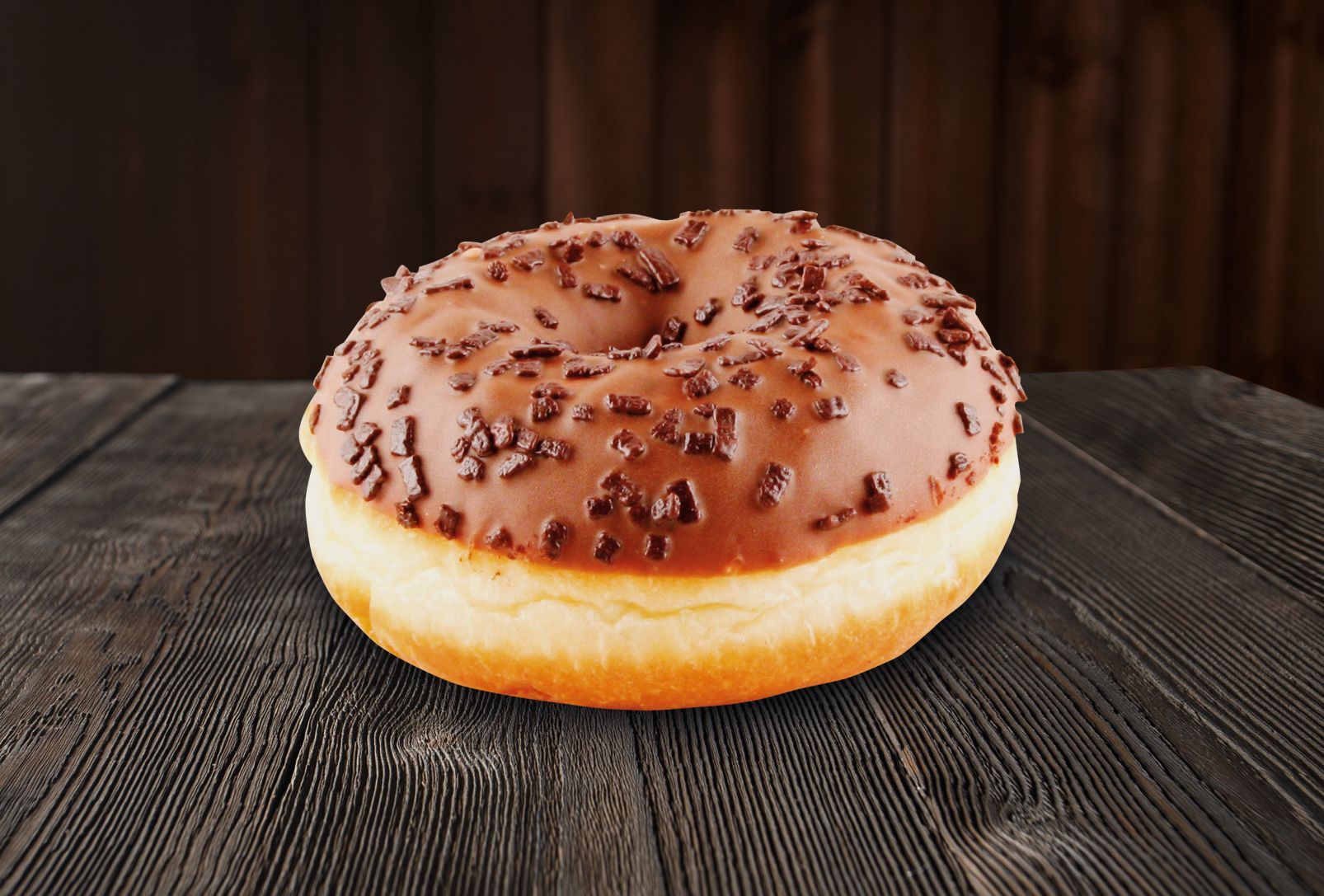 A chocolate donut is sitting on a wooden table.