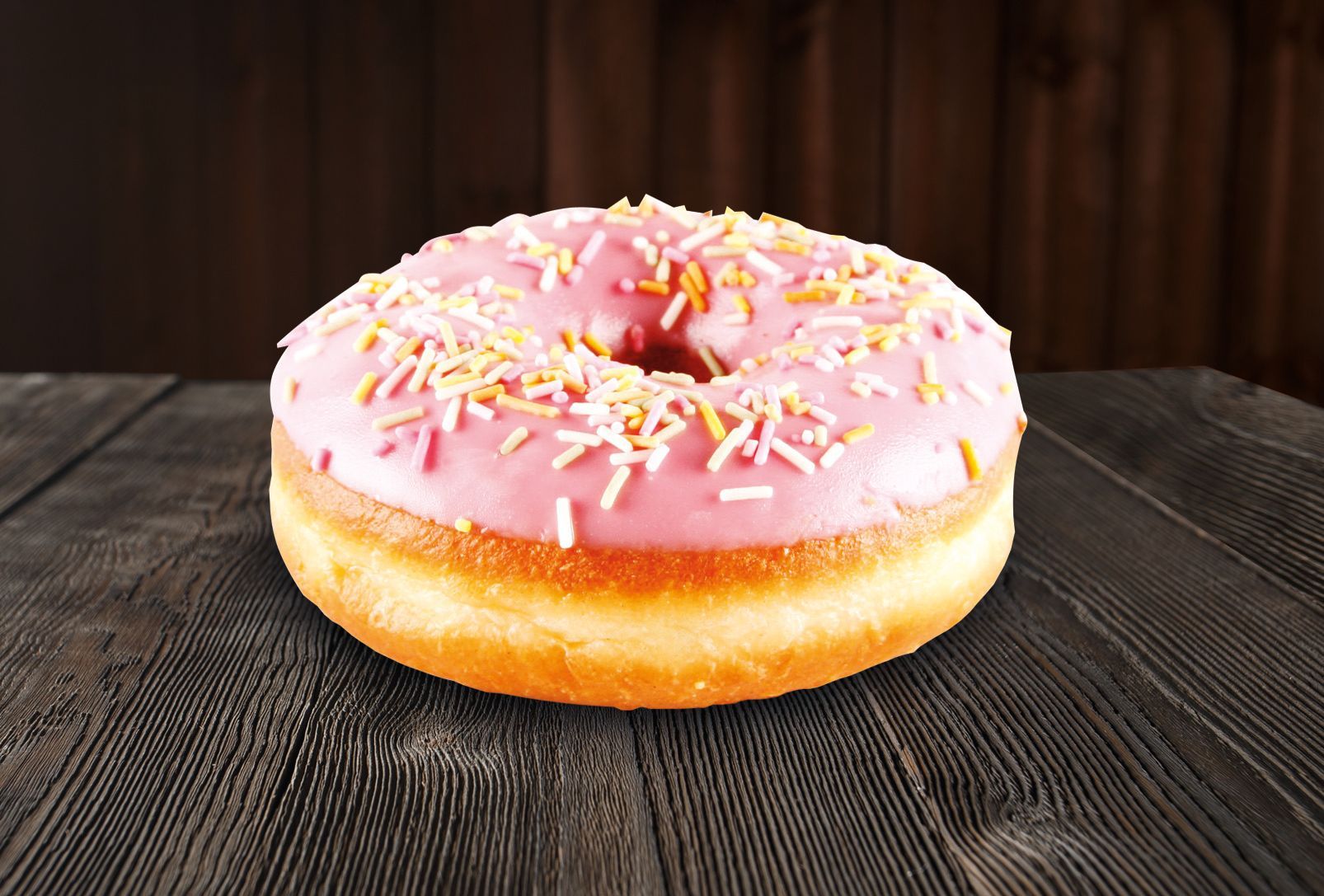 A donut with pink frosting and sprinkles on a wooden table.