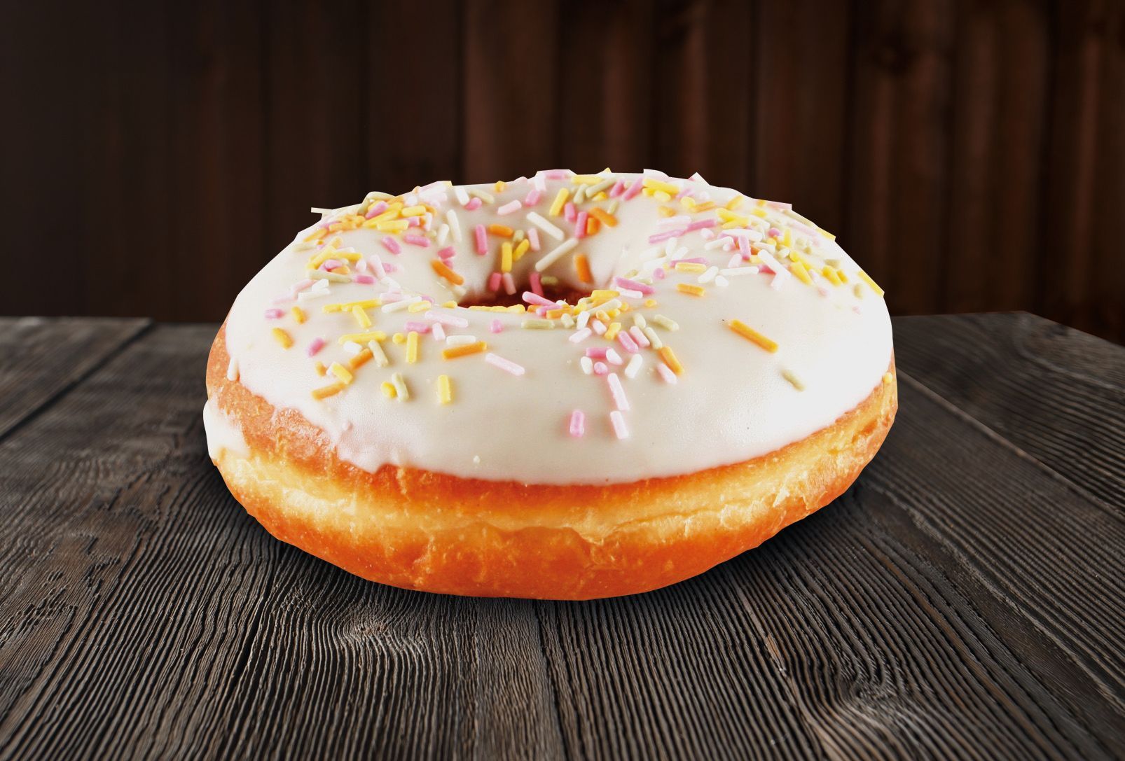 A donut with white frosting and sprinkles on a wooden table.