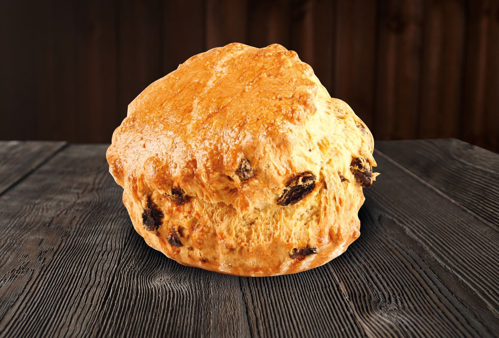 A raisin scone is sitting on a wooden table.