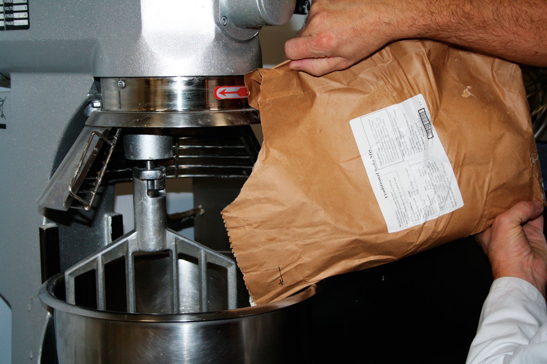 A person is pouring a bag of flour into a mixer
