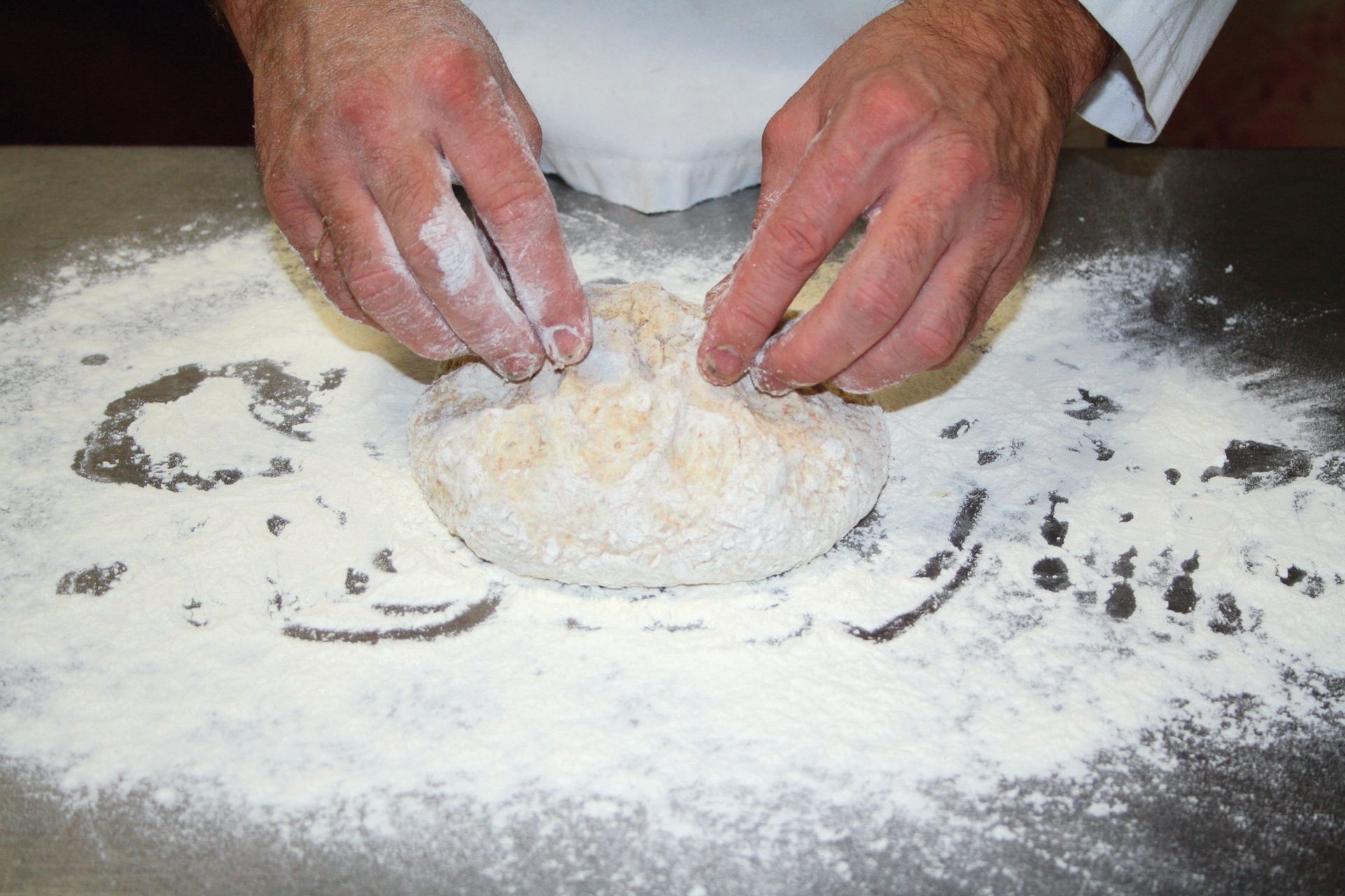 A person is kneading dough on a table covered in flour