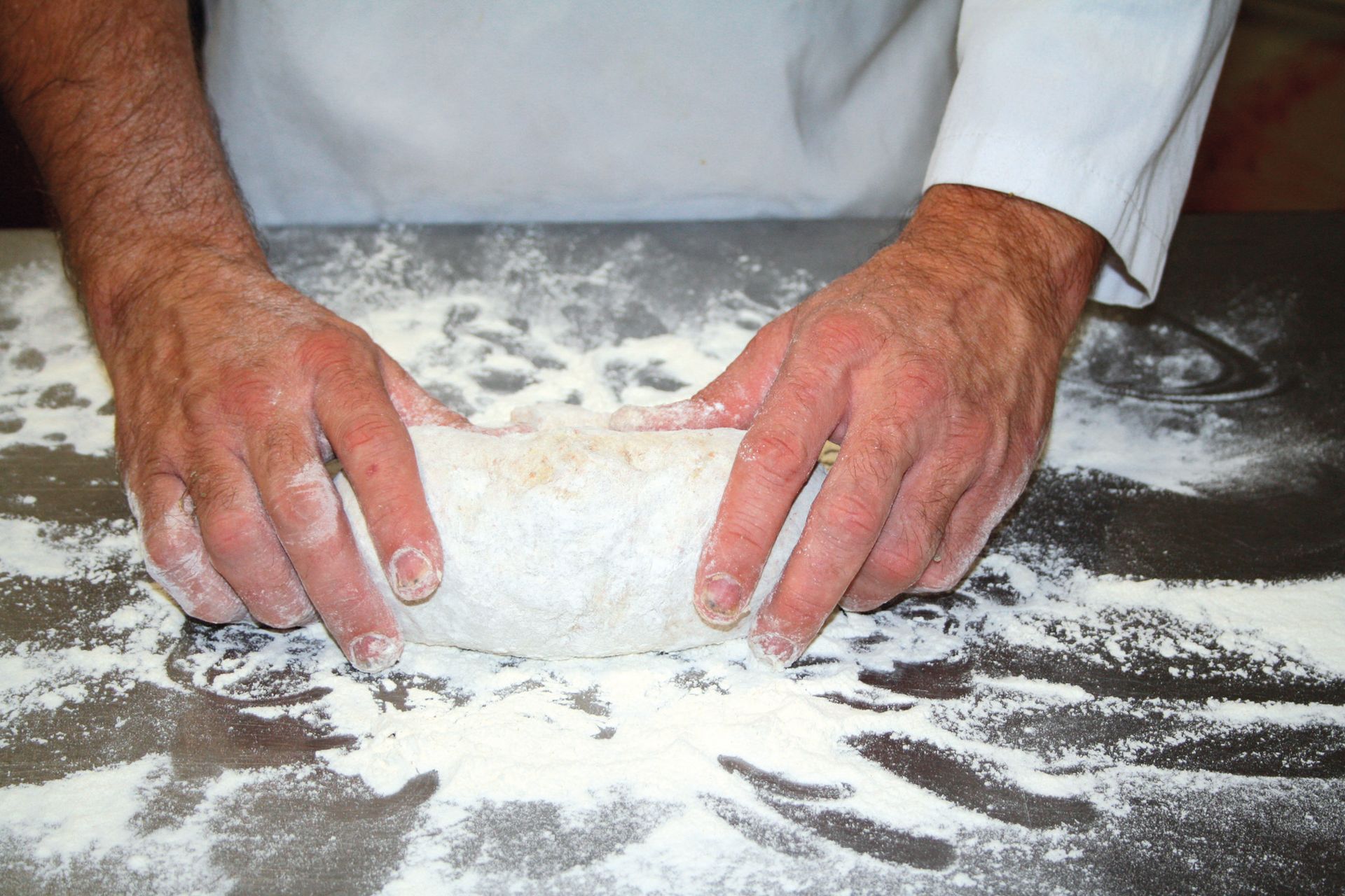 A person is kneading dough on a table covered in flour