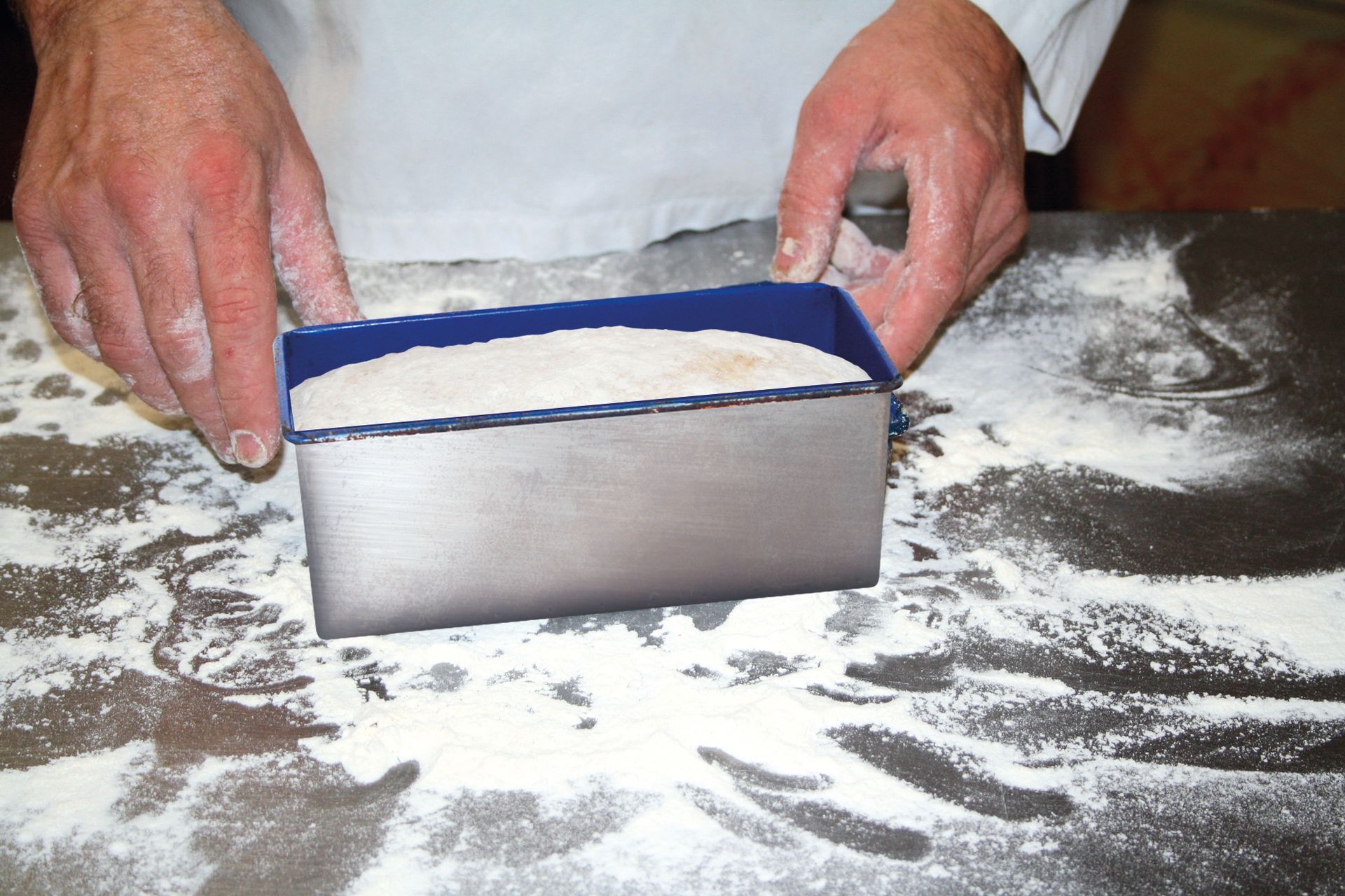 A person is making a loaf of bread in a metal pan