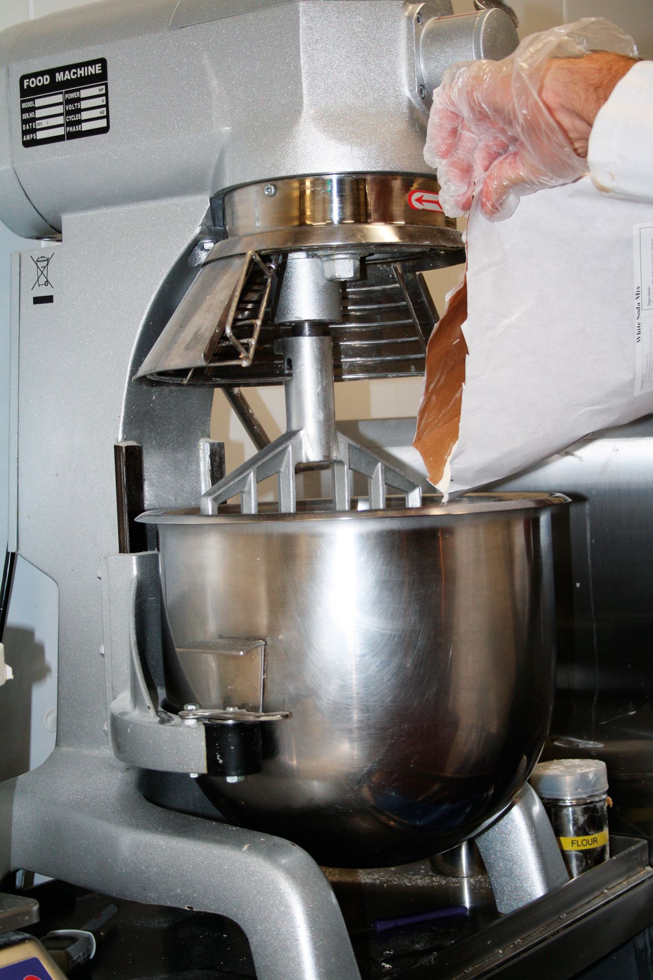 A person wearing gloves is pouring something into a mixer