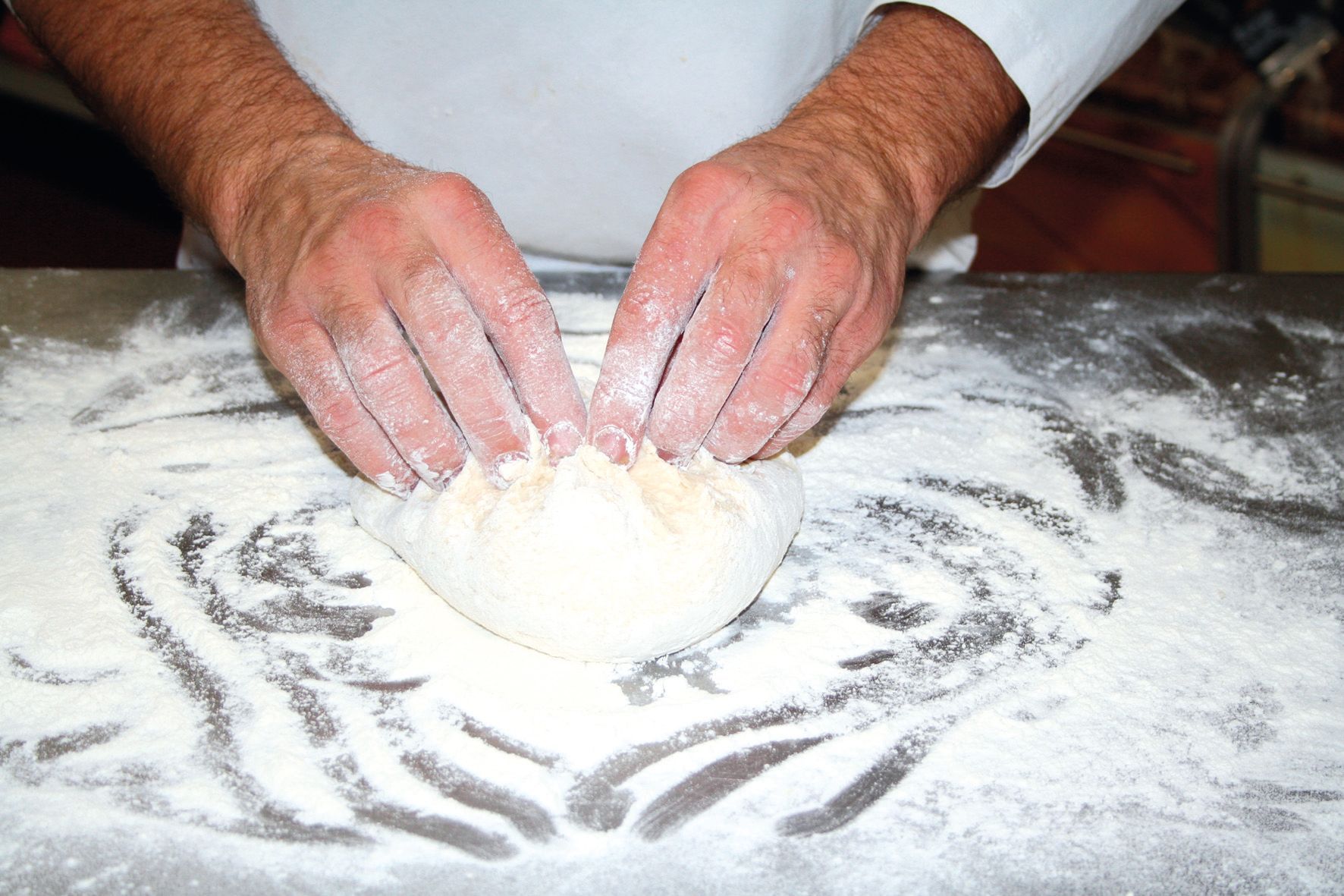 A person is kneading a ball of dough on a table
