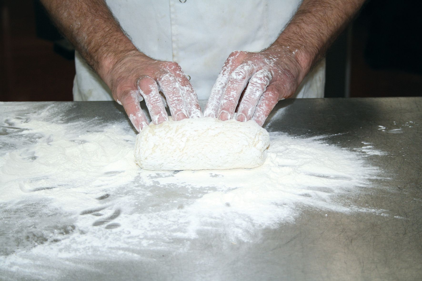 A person is kneading dough on a table covered in flour