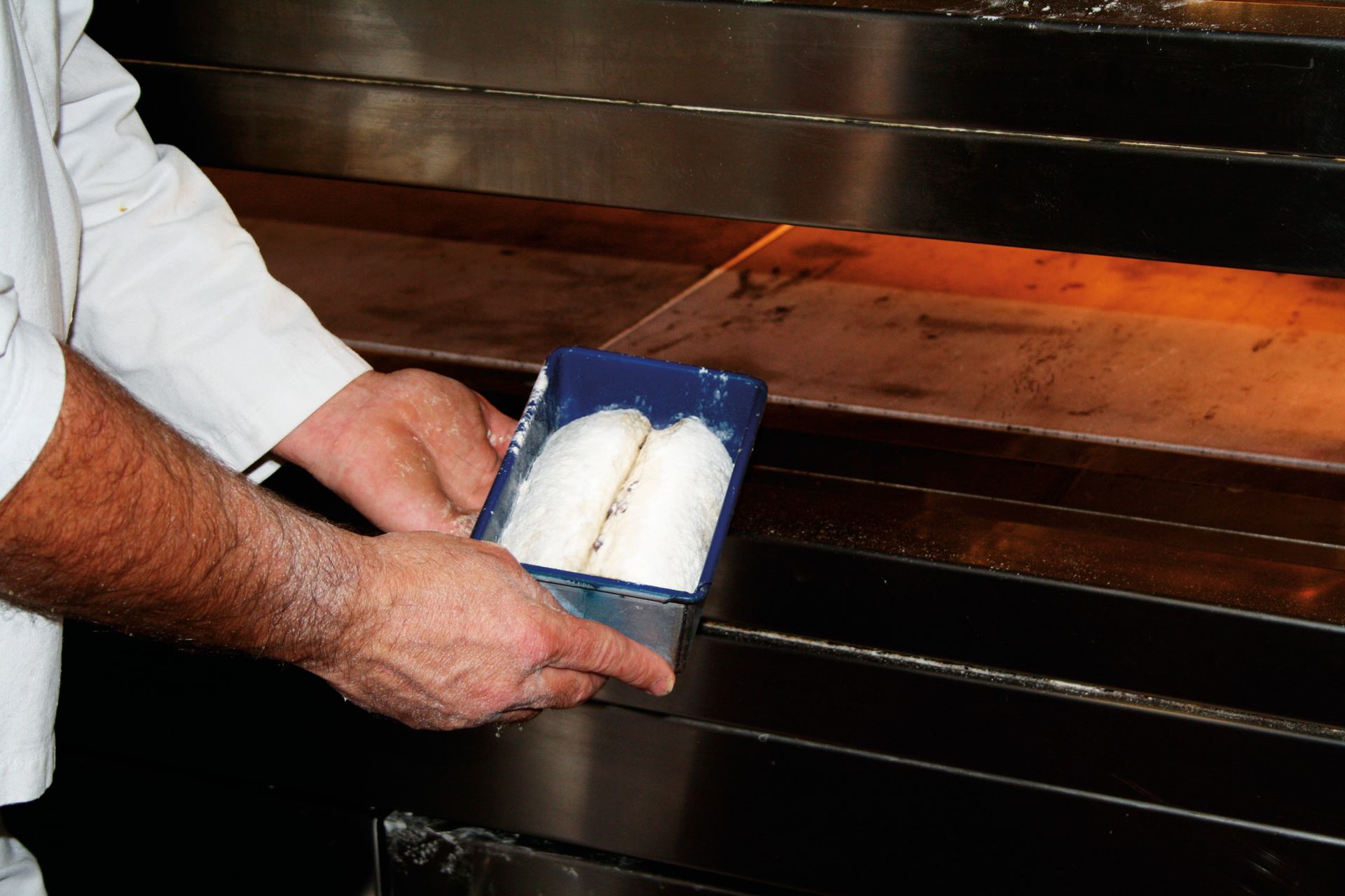 A man is holding a tray of food in front of an oven