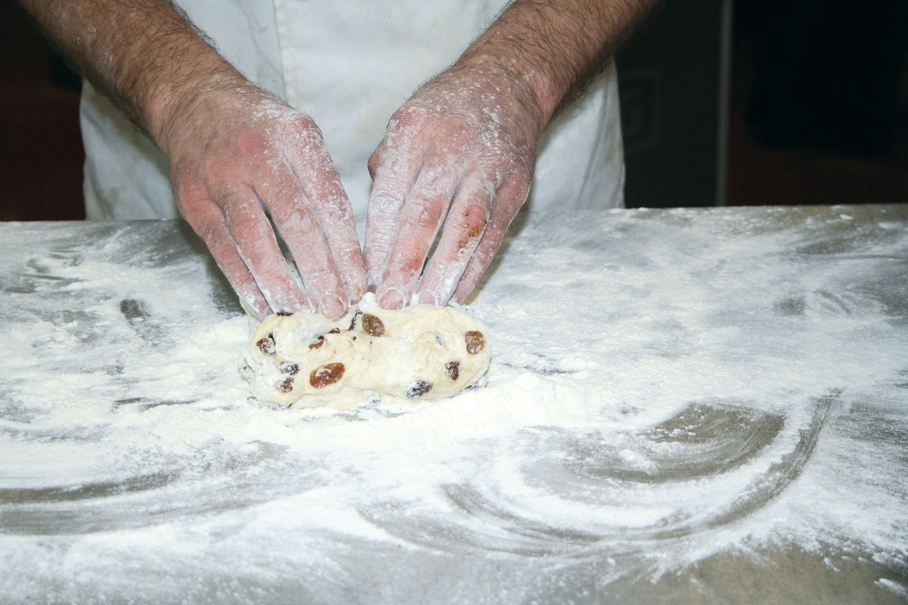 A person is kneading a piece of dough on a table covered in flour.