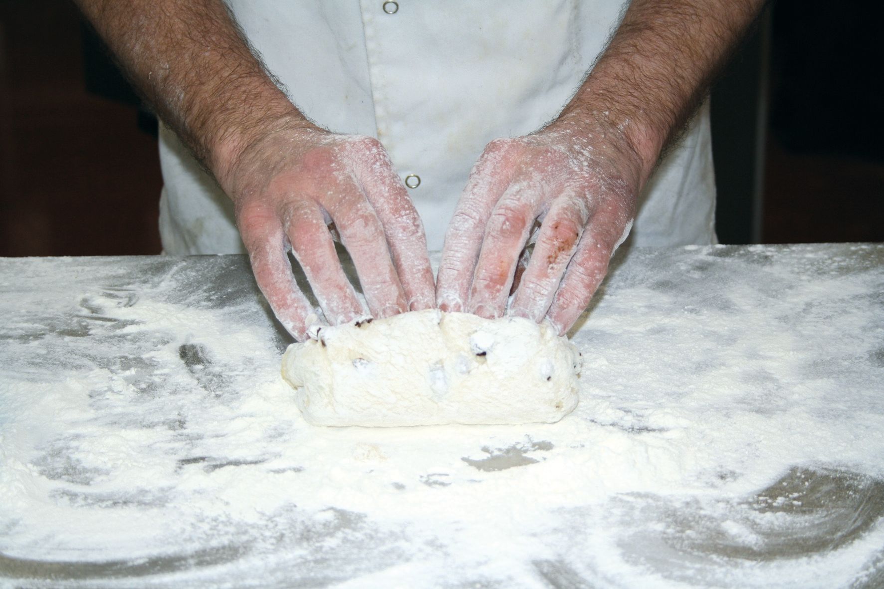 A person is kneading a piece of dough on a table covered in flour.