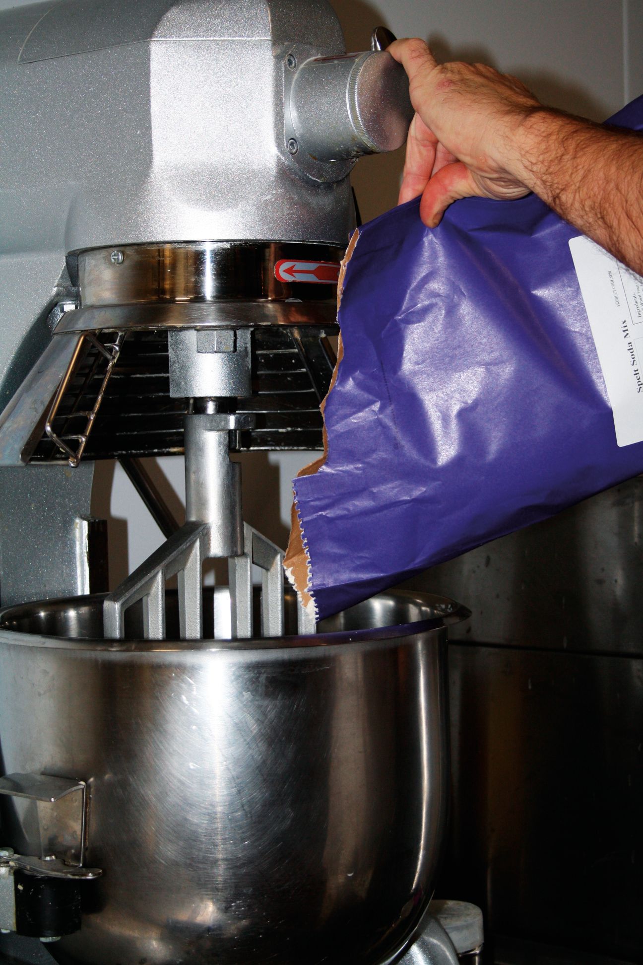 A person is pouring a bag of flour into a mixer