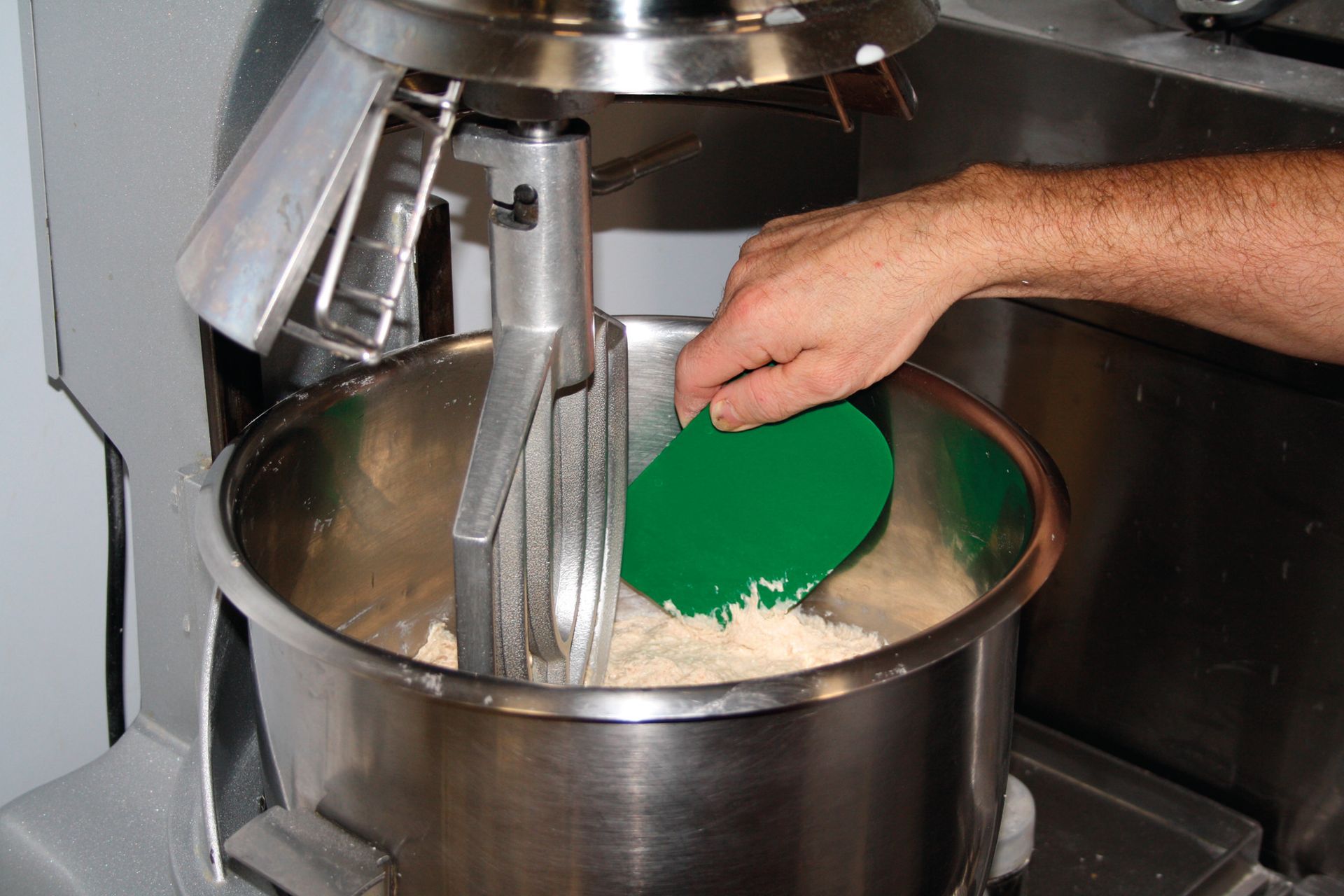 A person is using a green spatula to mix something in a mixer