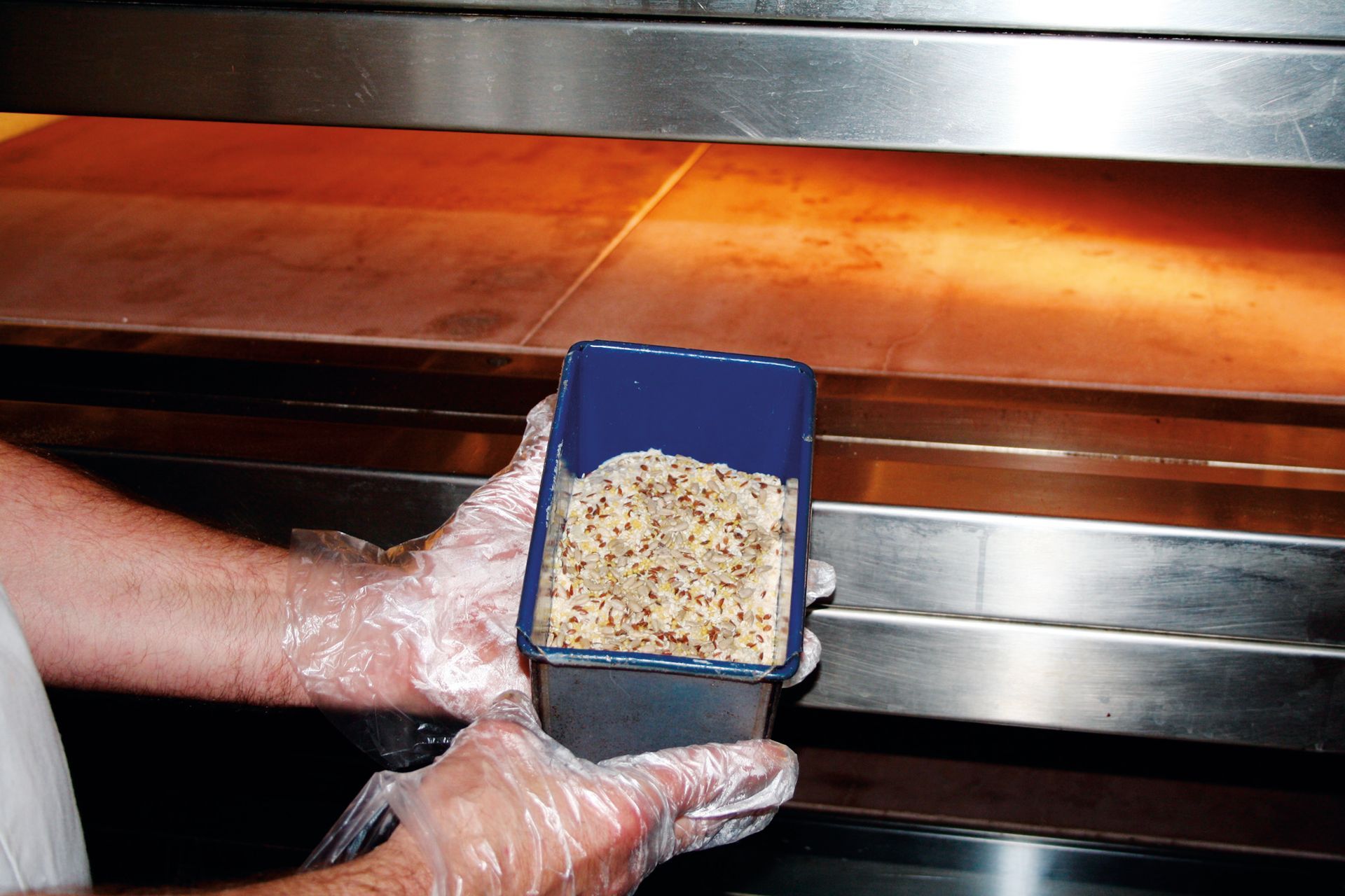 A person wearing plastic gloves is holding a container of food in front of an oven