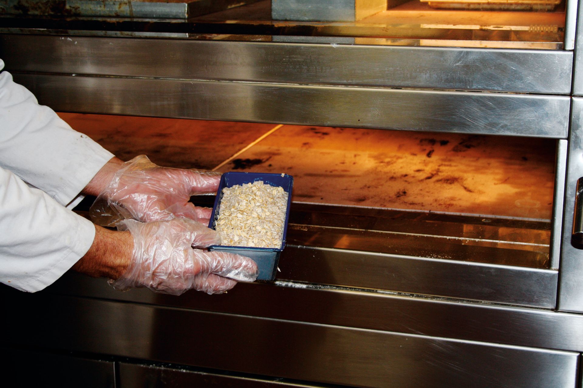 A person wearing plastic gloves is putting food into an oven