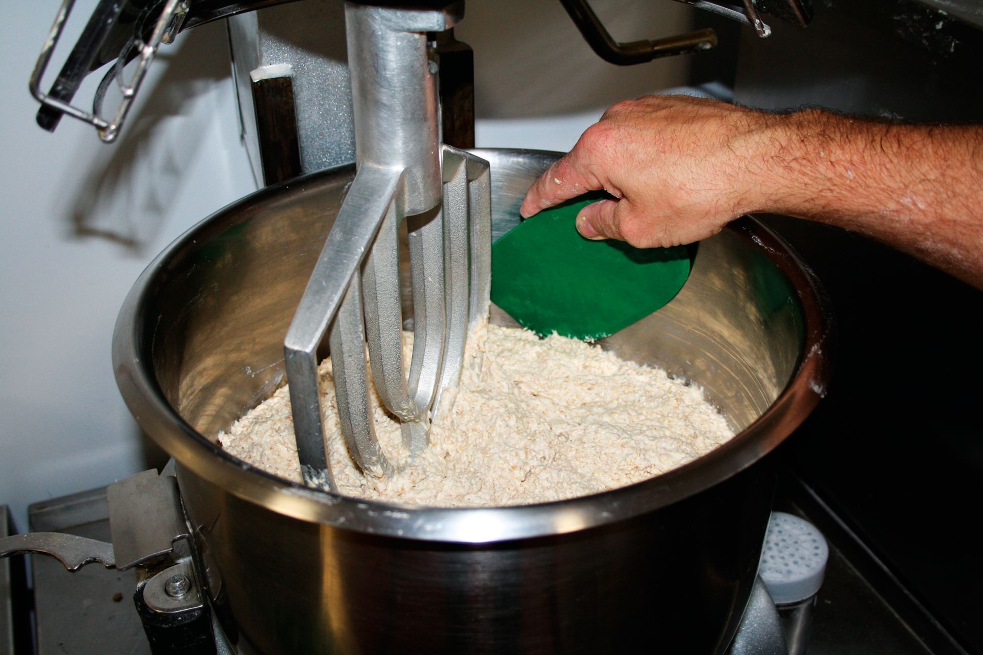 A person is using a green spatula to mix ingredients in a mixer