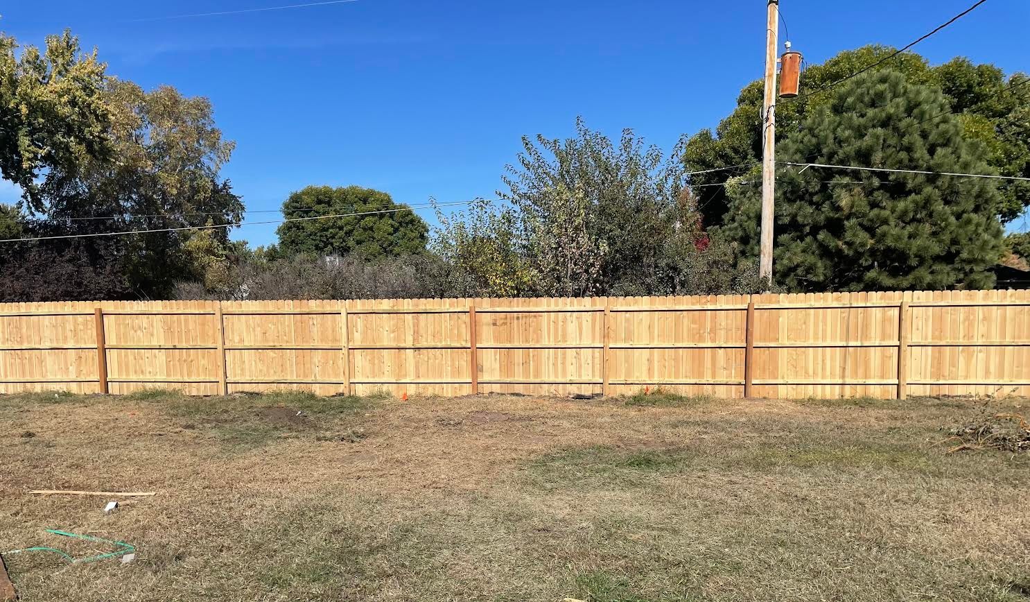 A wooden fence surrounds a grassy field with trees in the background.