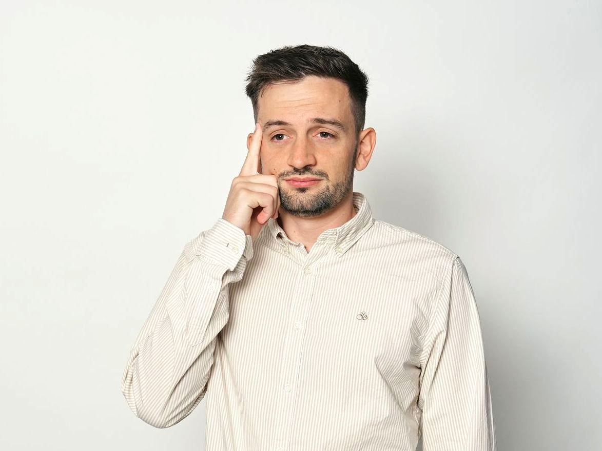 A man in a striped shirt is holding his hand to his forehead.