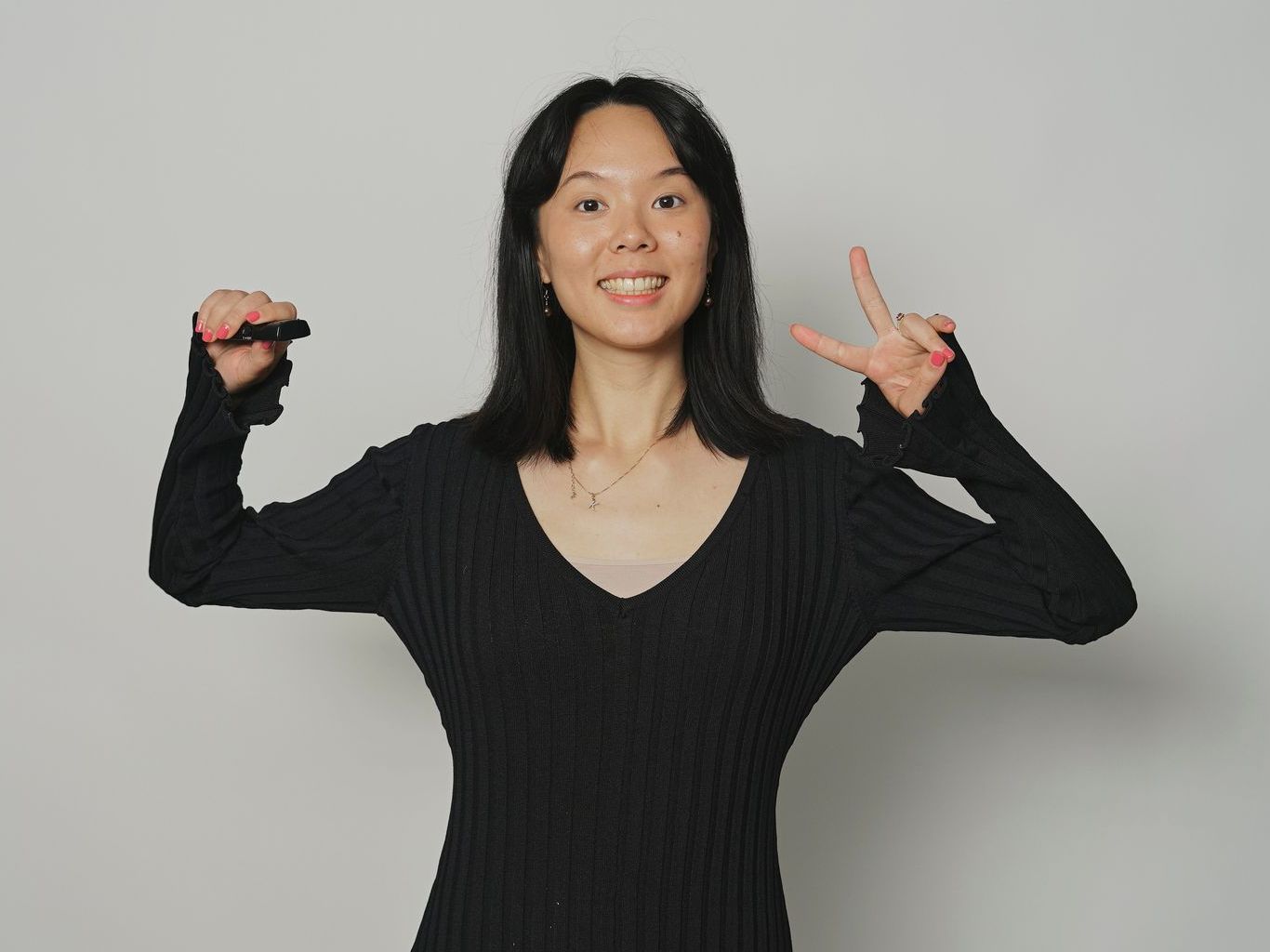 A woman in a black sweater is making a peace sign with her hands.