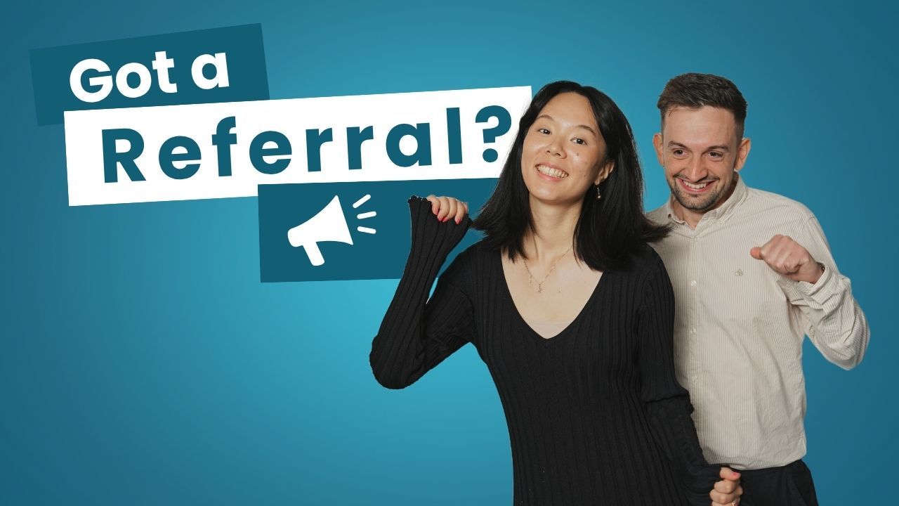 A man is standing next to a woman sitting in front of a computer.