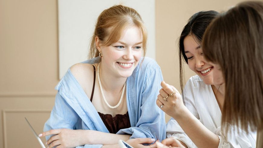Three women are sitting at a table looking at a laptop.