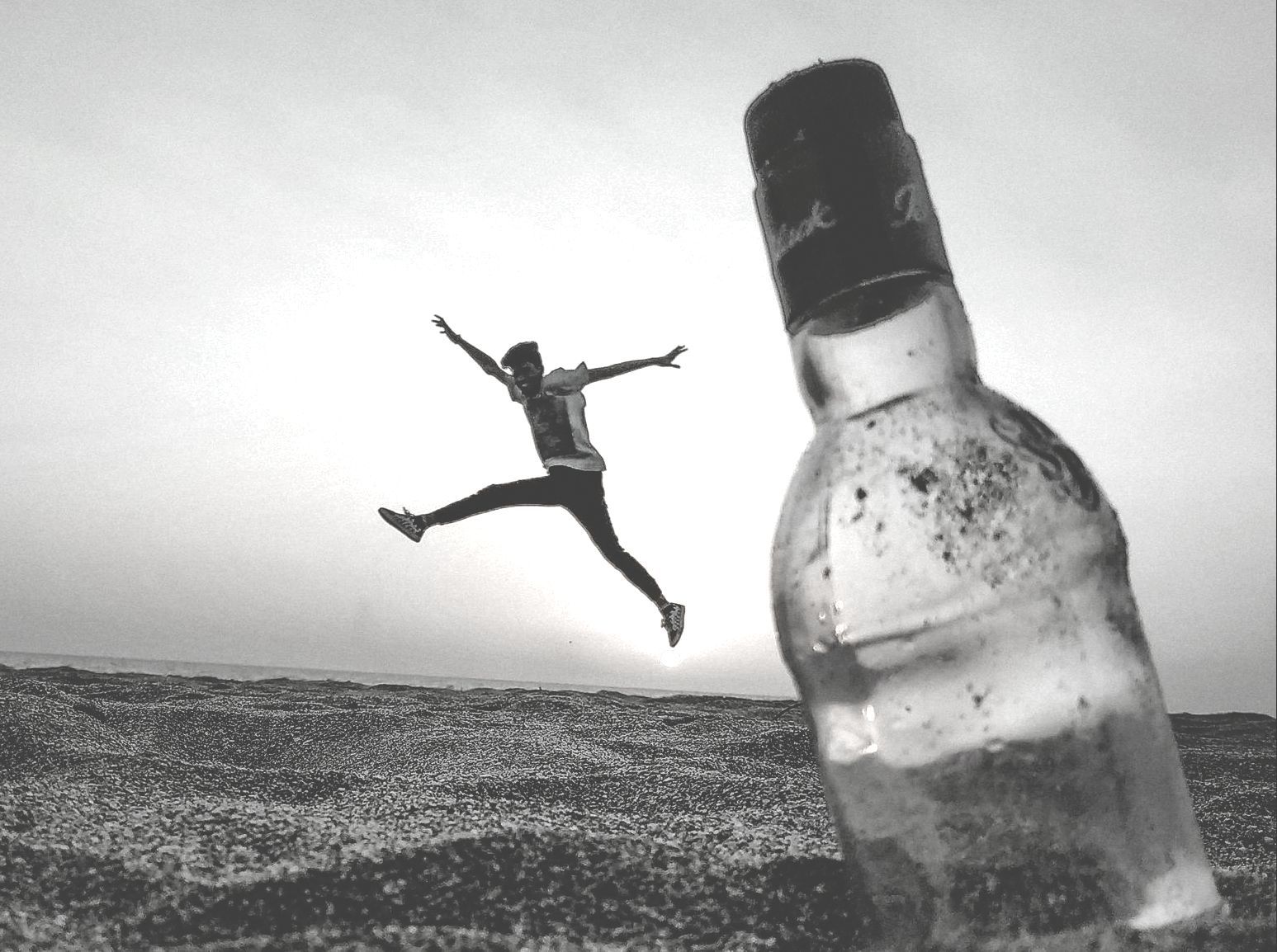A person is jumping in the air next to an empty bottle