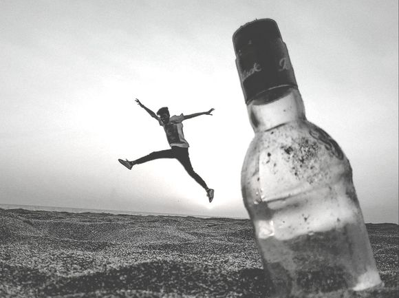 A person is jumping in the air next to an empty bottle