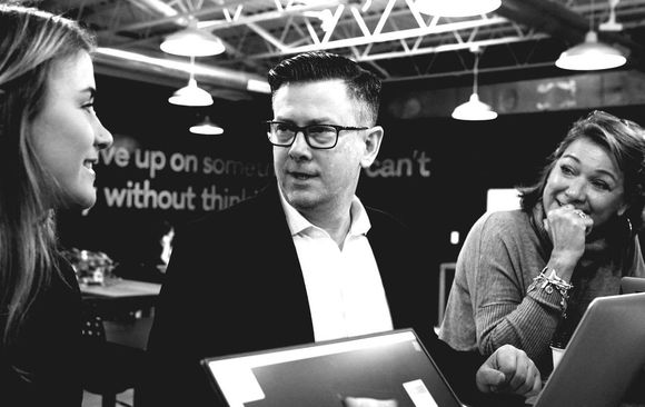 A group of people are sitting around a table looking at a laptop.